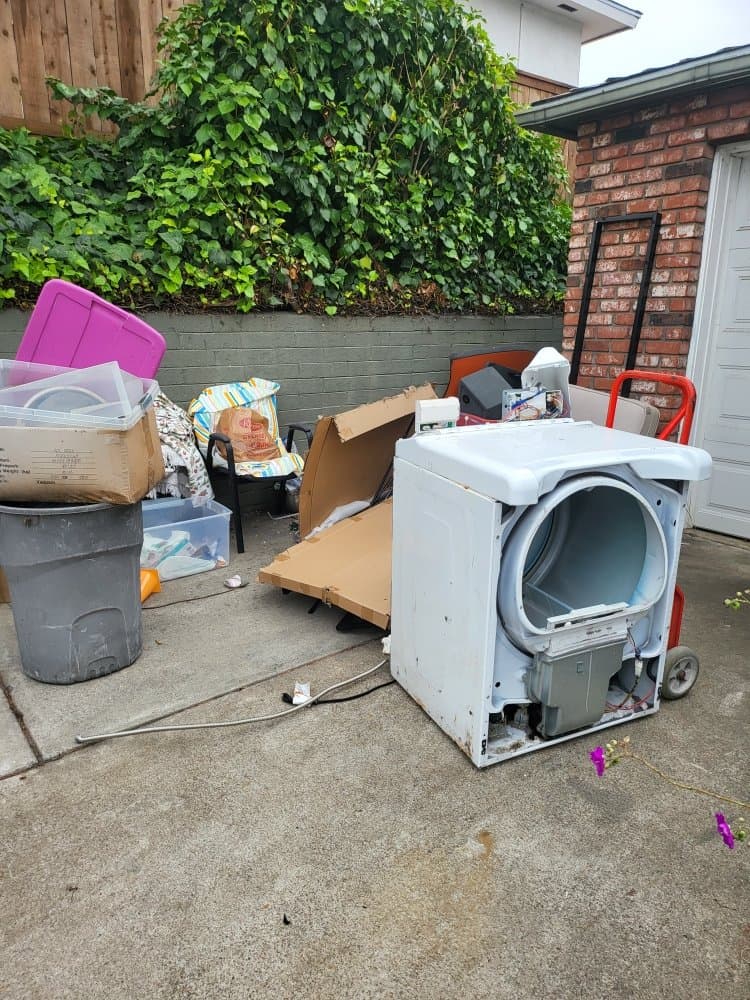 San Diego driveway piled with an old dryer, broken furniture, and boxes before junk removal